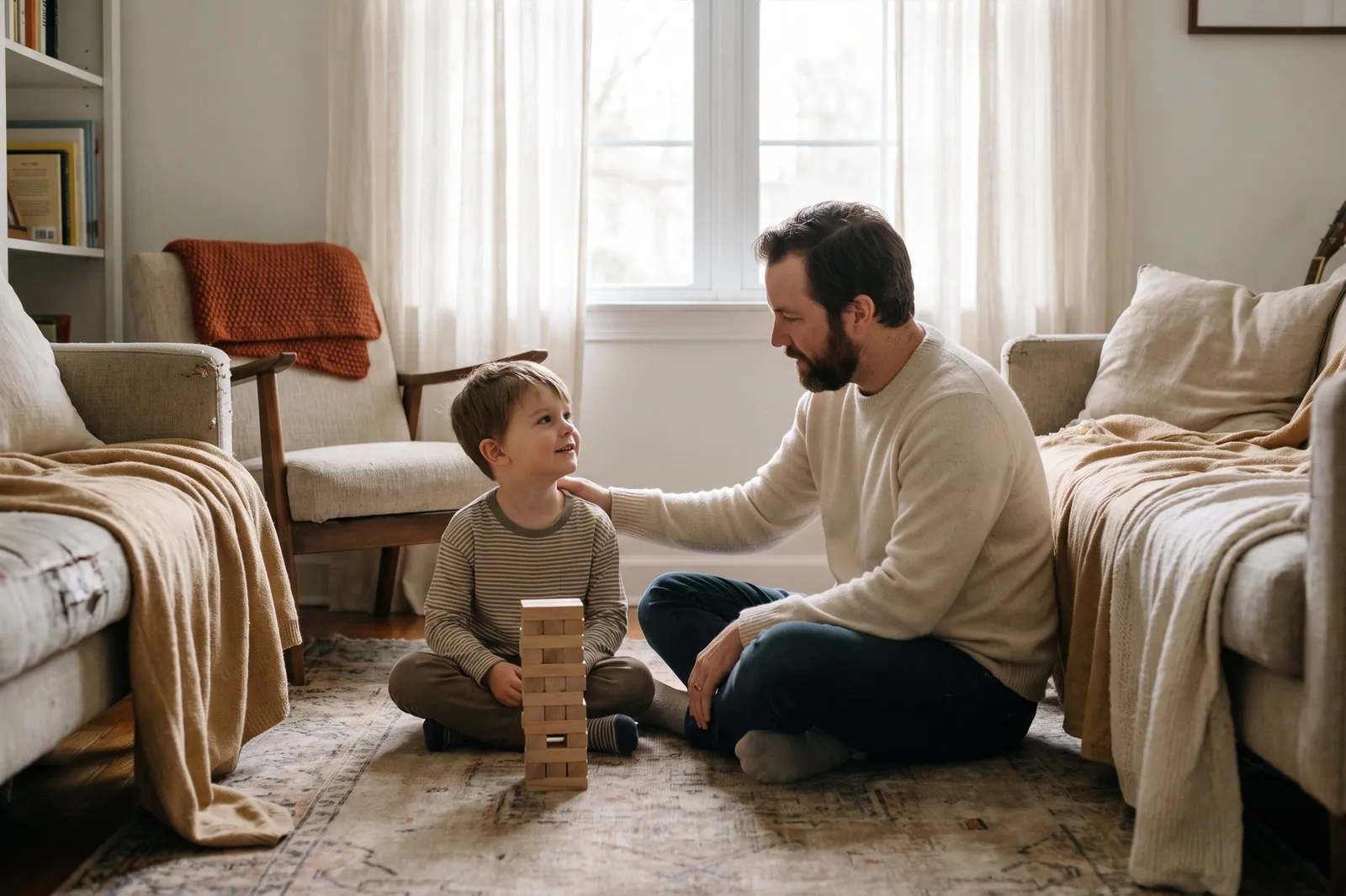 A father gently touches his son's shoulder as the boy looks up from his block tower