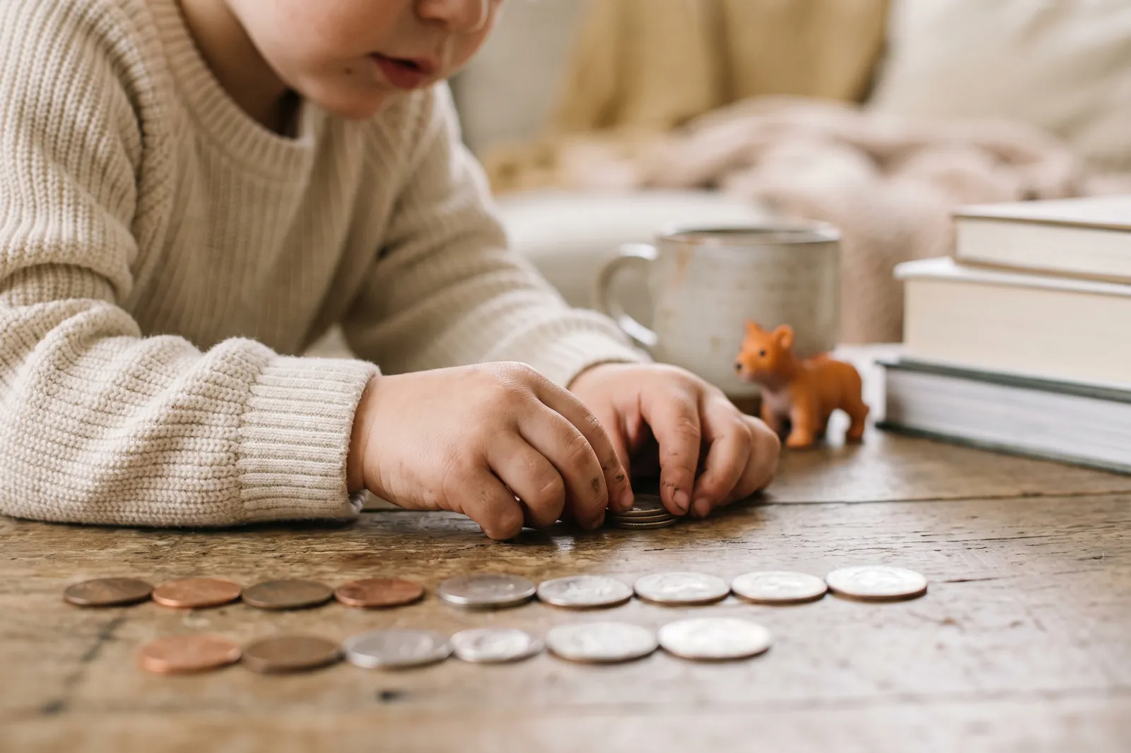 A child's hands line up coins in rows by size on a wooden table